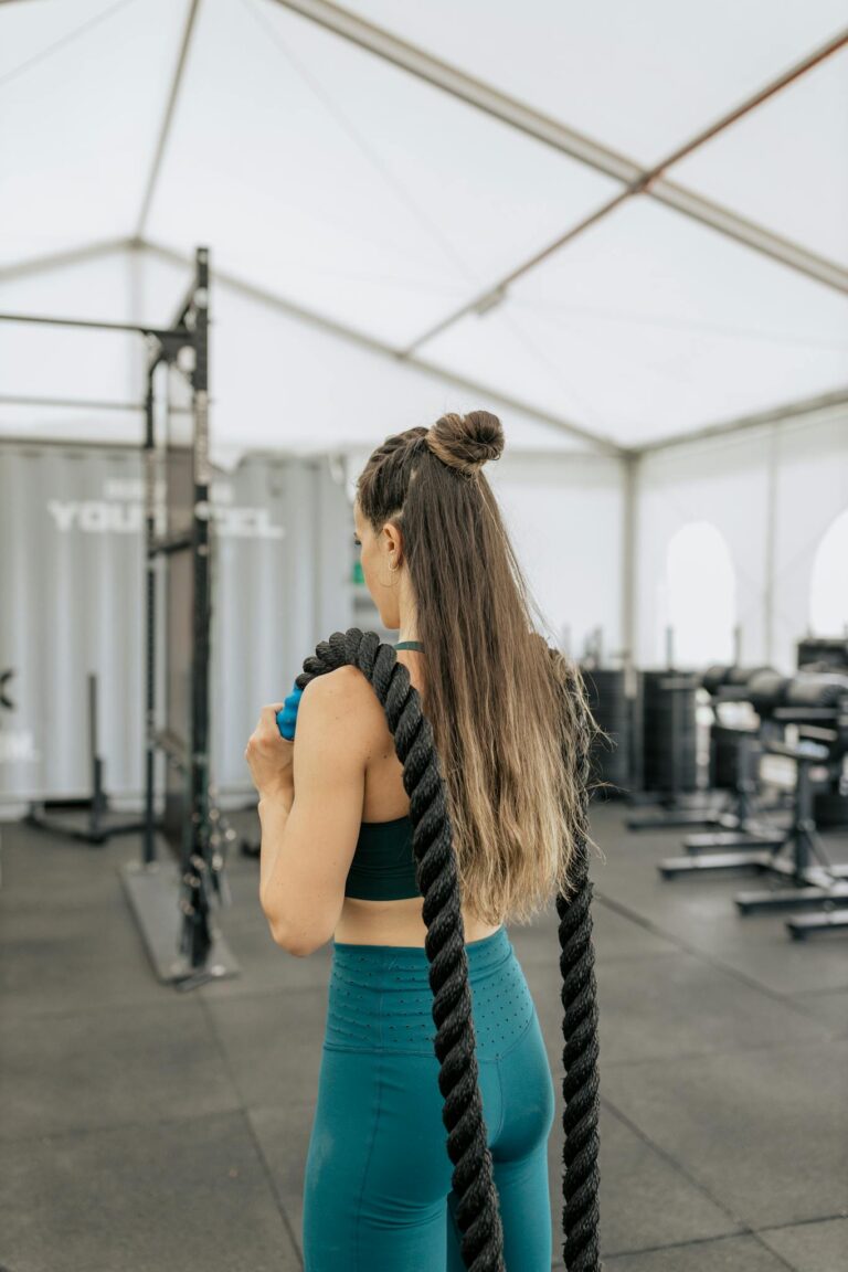 Fit woman in activewear using battle ropes indoors for a workout.