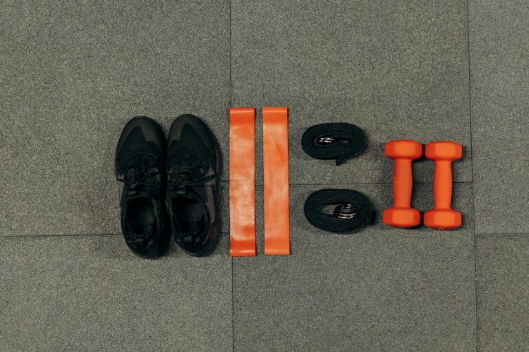 Flat lay of gym essentials including dumbbells, sneakers, and resistance bands on a grey floor.