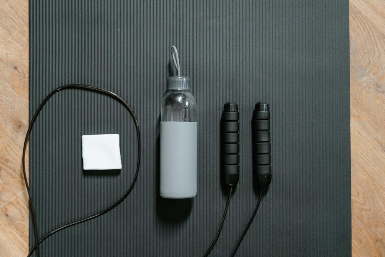 Flatlay of jump rope, water bottle, and towel on a black yoga mat.