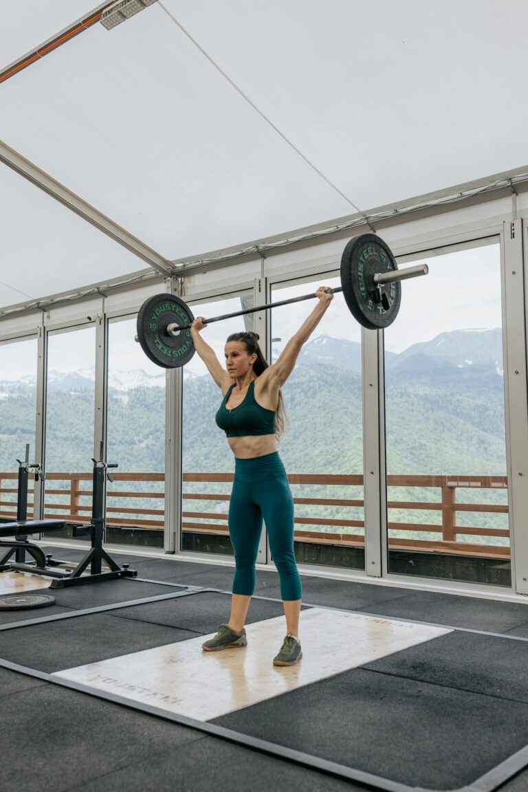 Strong woman weightlifting in an indoor gym with scenic mountain views.